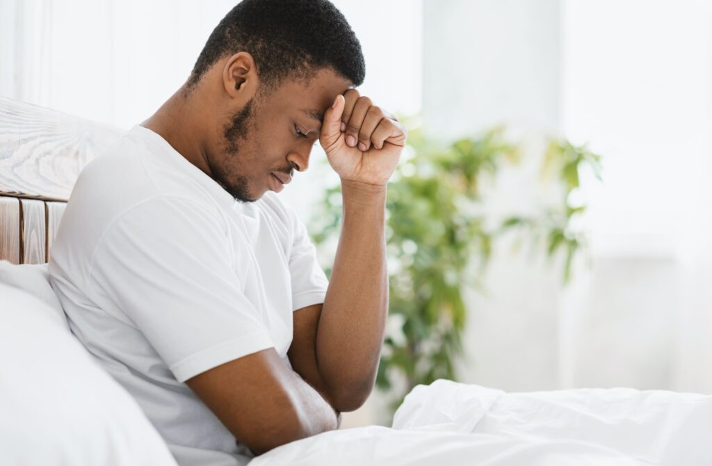 African American Man Suffering Depression Sitting In Bed At Home