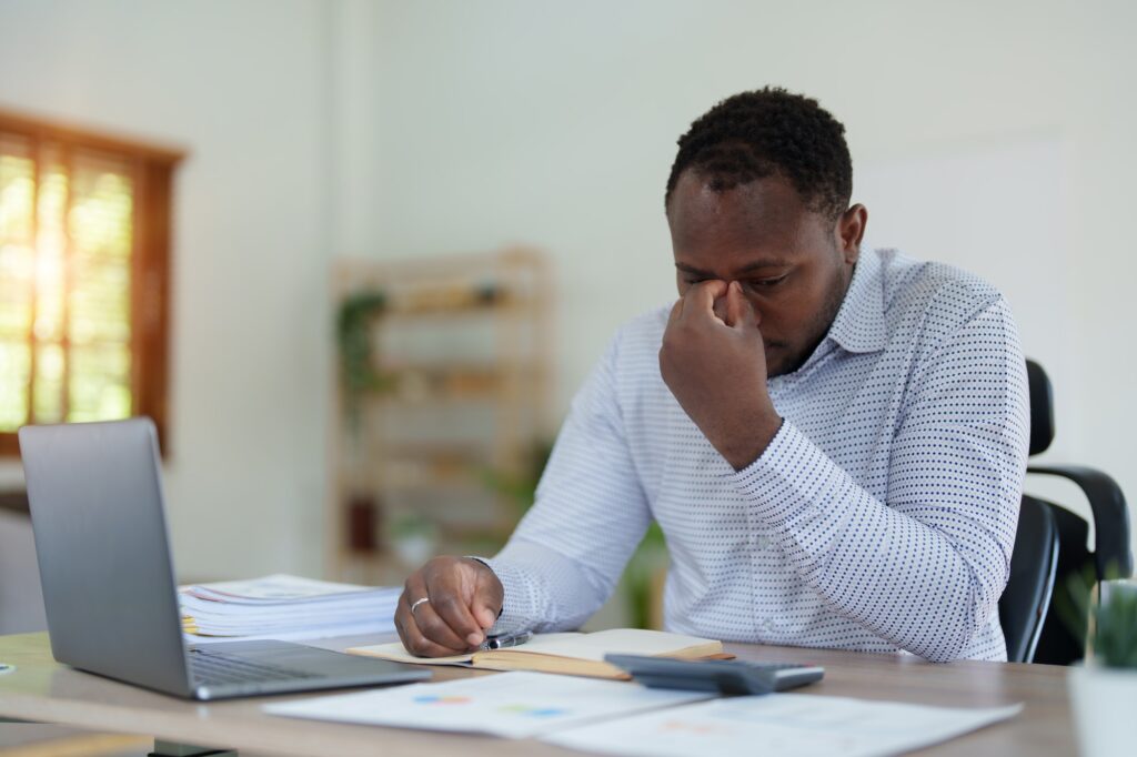 Burnout American African business man in stress works with many paperwork document, migraine attack,