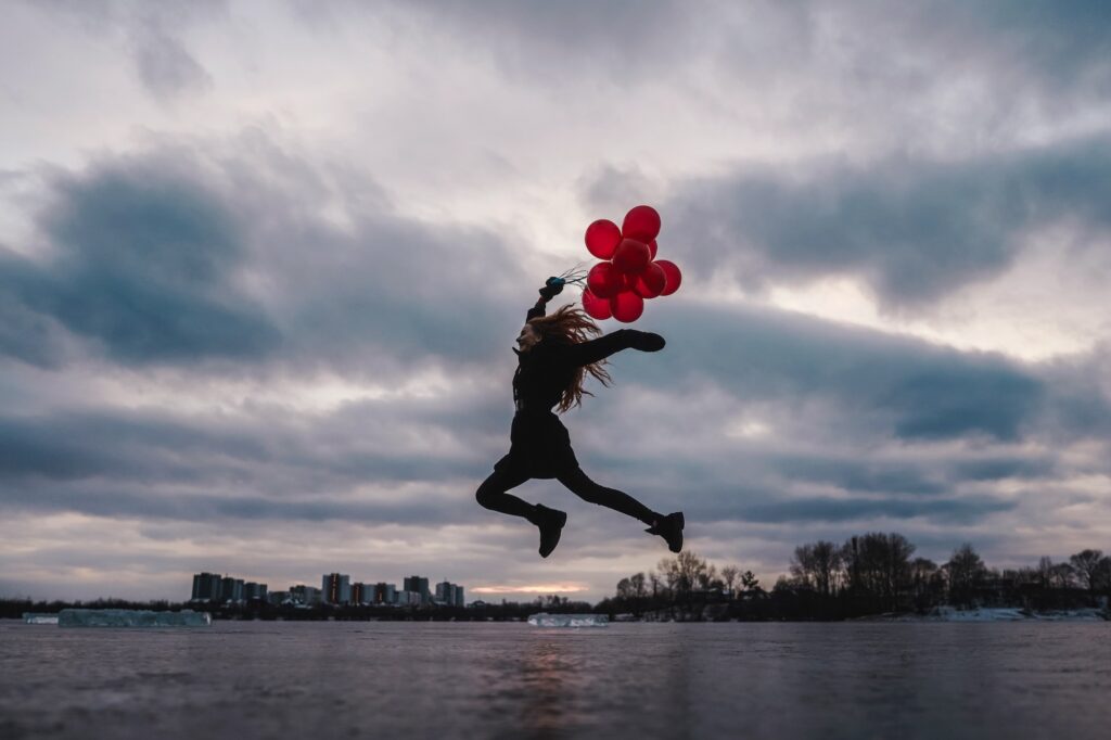 Imagination, happy girl jumping with red balloons at sunset on the frozen river, follow your dream.