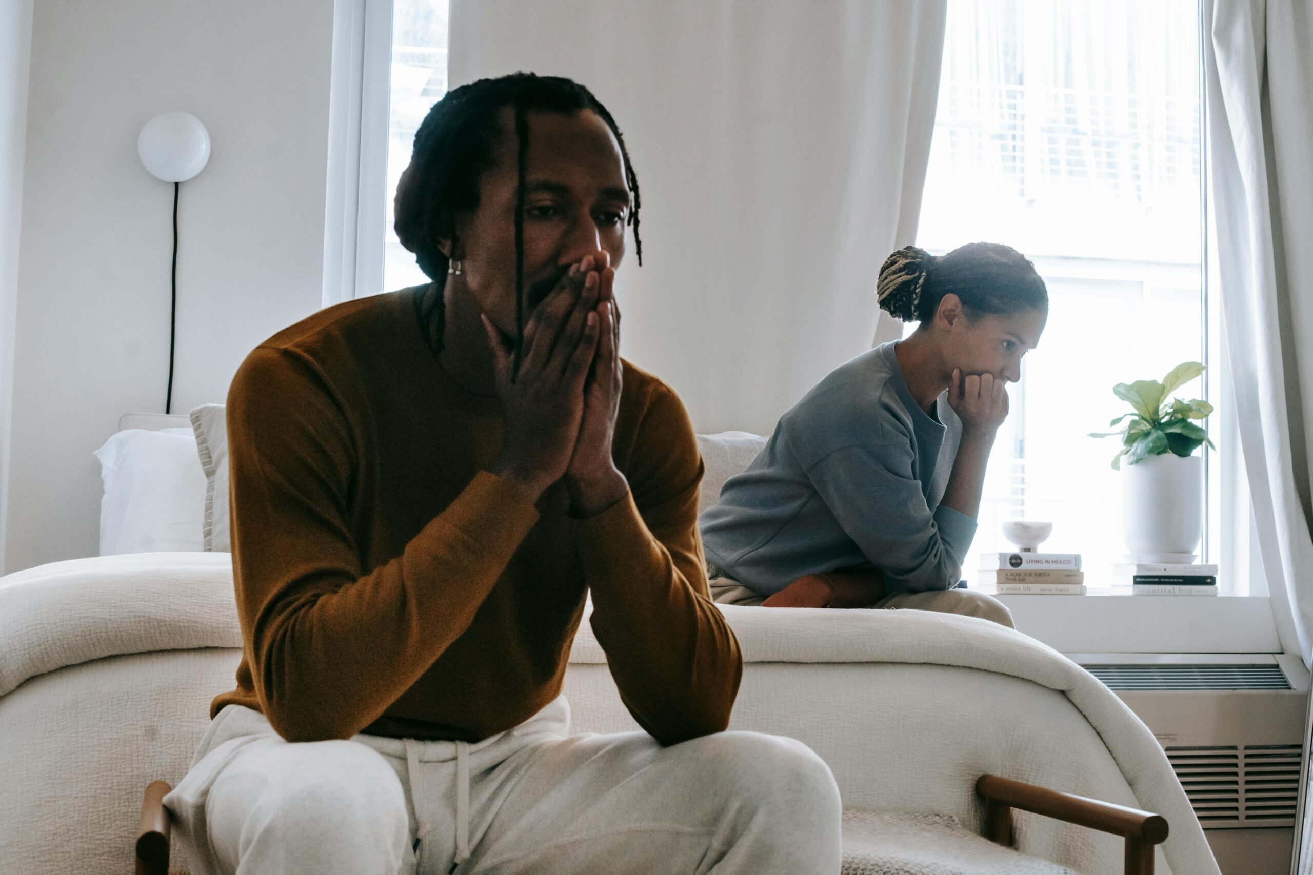 man and woman sitting on opposite ends of bed upset